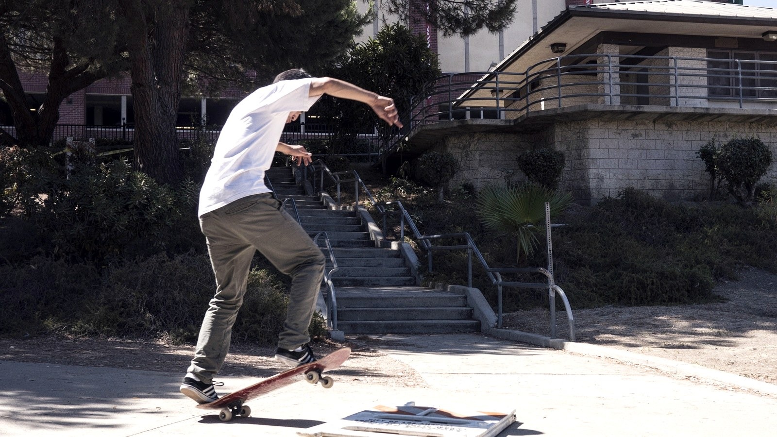 Skateur en manual sur le parking d'un lycée de Los Angeles, escalier et rampe en arrière-plan
