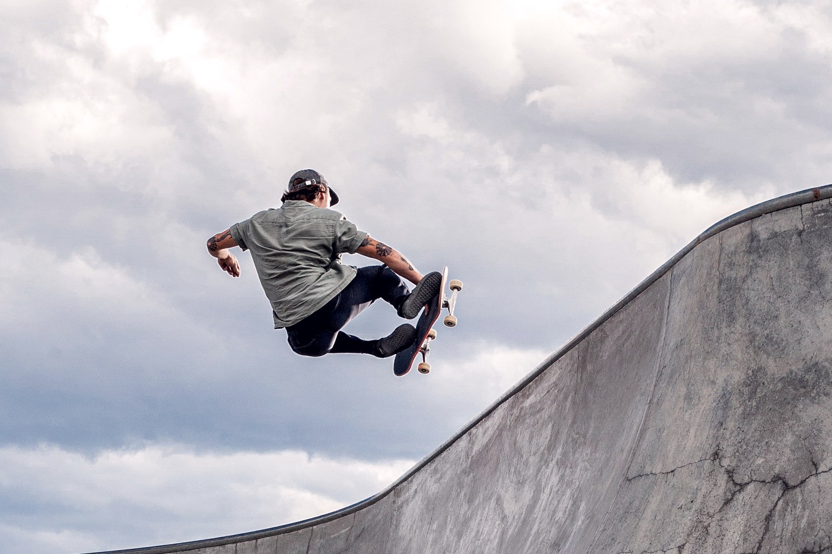 Skateur en frontside air au-dessus du coping d'un bowl en béton fissuré, ciel chargé
