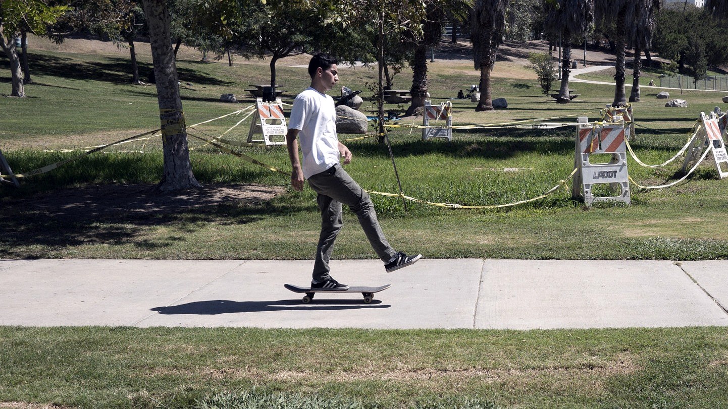 Skateur en session sur un trottoir de Los Angeles, palmiers et skyline du centre-ville en fond