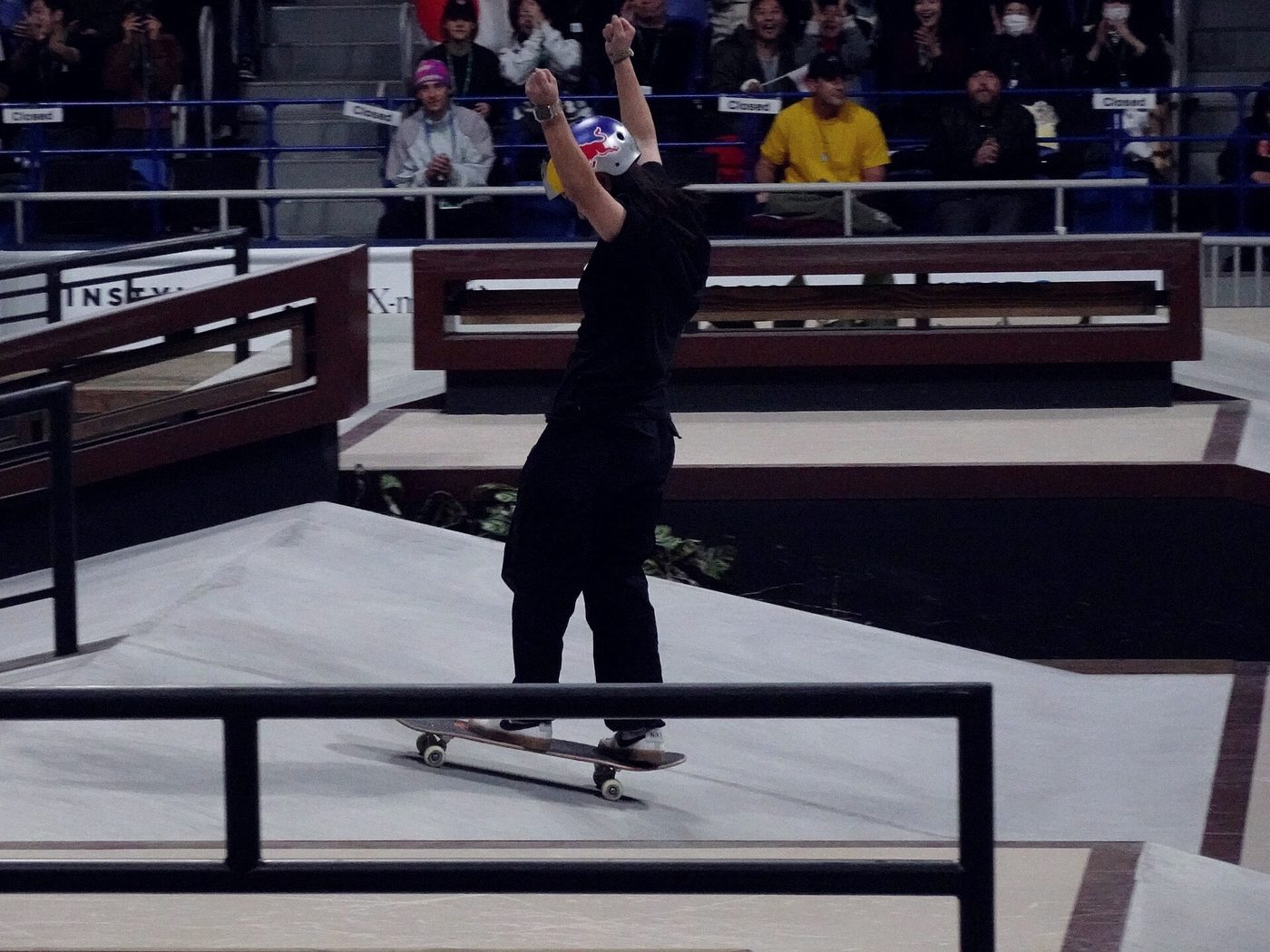 Skateuse bras levés après sa figure en finale de street, tribunes pleines derrière elle