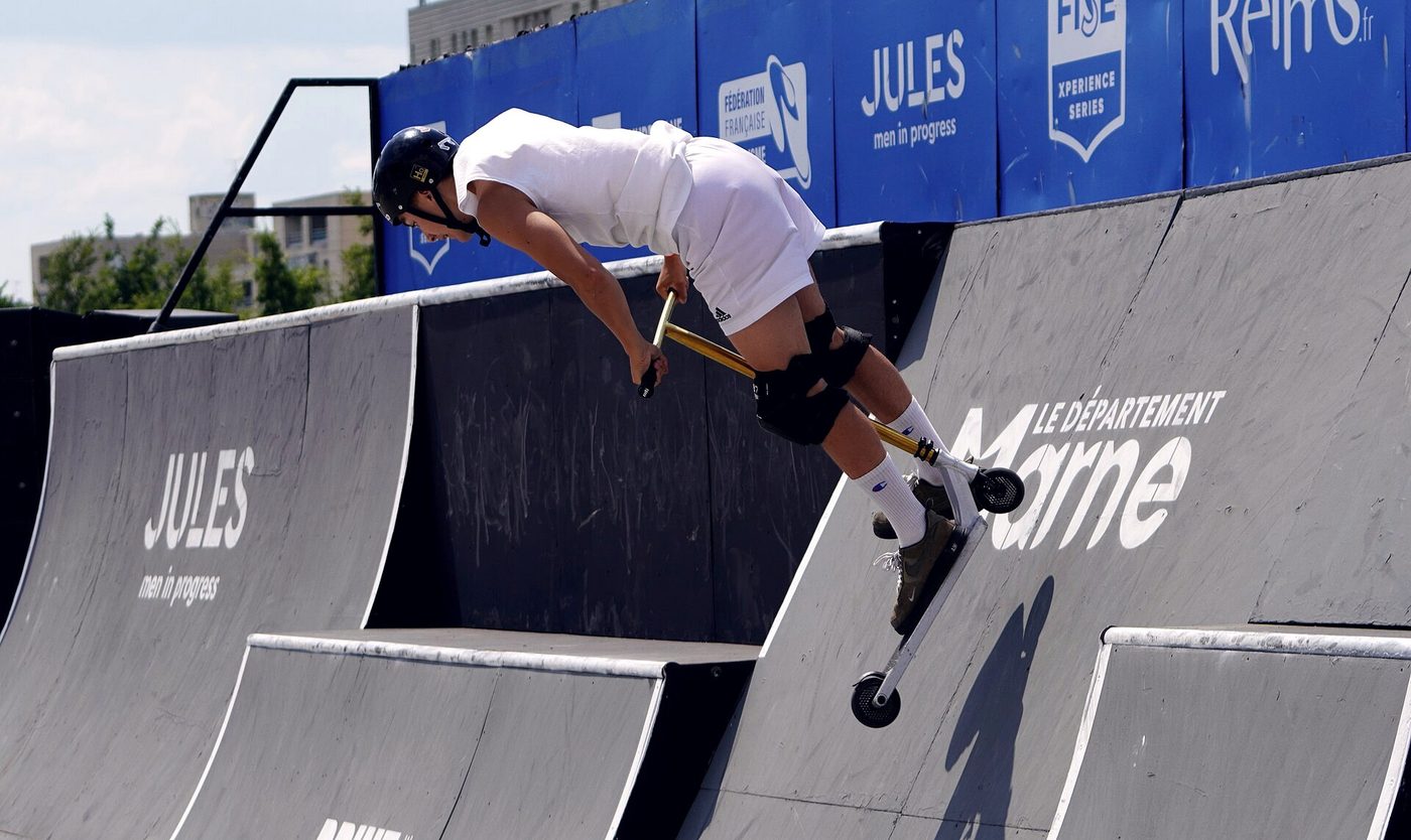Rider de trottinette freestyle en l'air au-dessus des modules d'une étape FISE, panneau FISE Xperience Series au fond