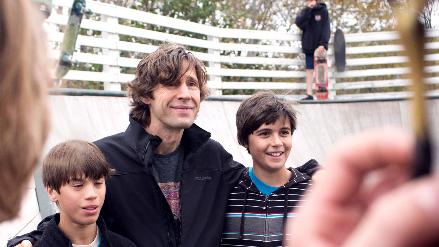 Rodney Mullen souriant entouré de deux jeunes skateurs au bord d un bowl