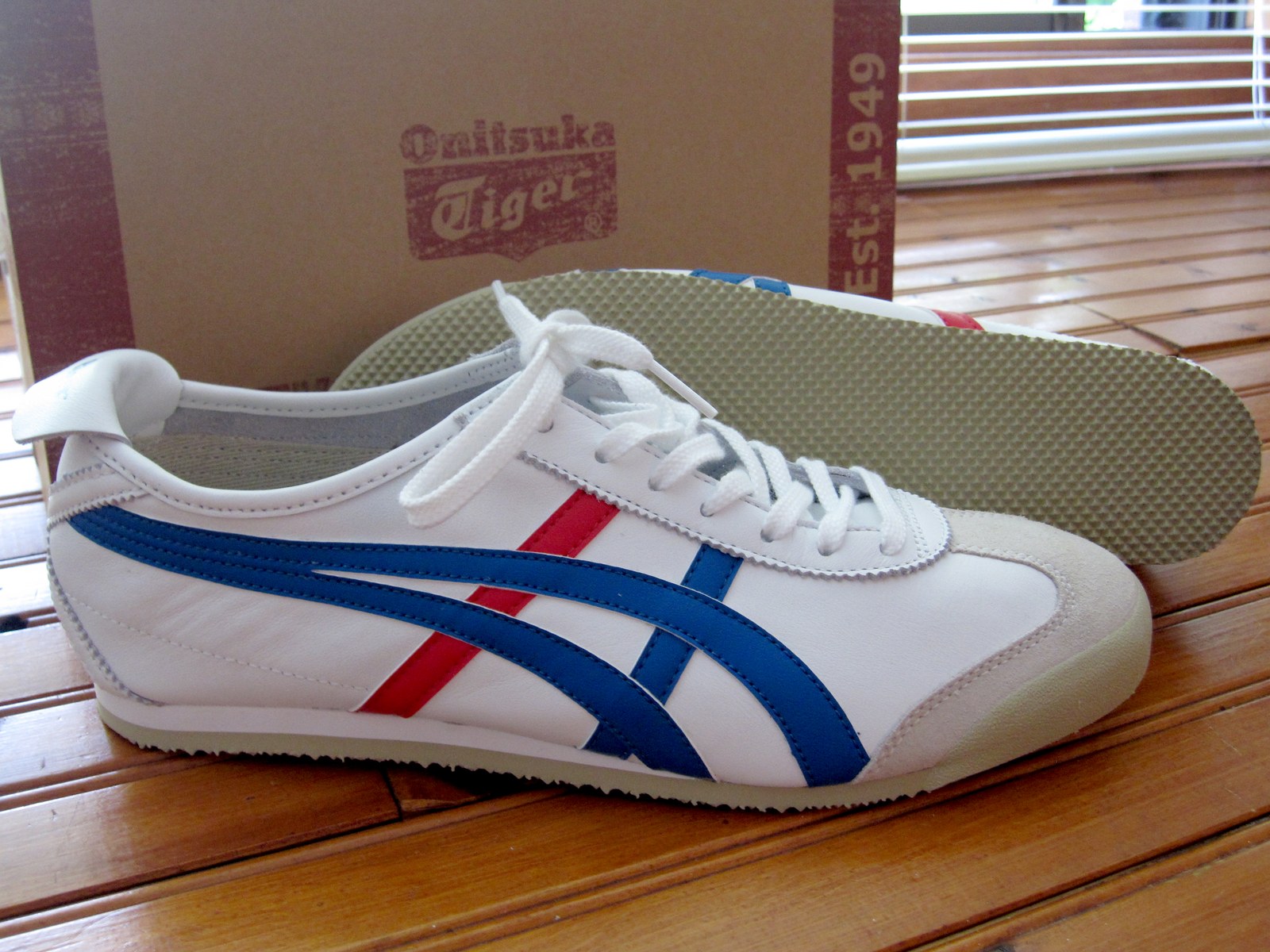 Chaussure Onitsuka Tiger Mexico 66 blanche à bandes bleues devant sa boîte marquée Est. 1949