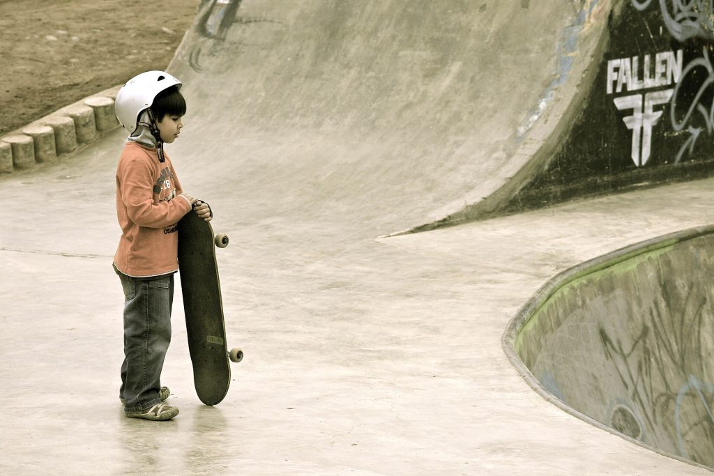 Jeune skateur casqué, board en main, au bord d’un bowl de skatepark avant de dropper