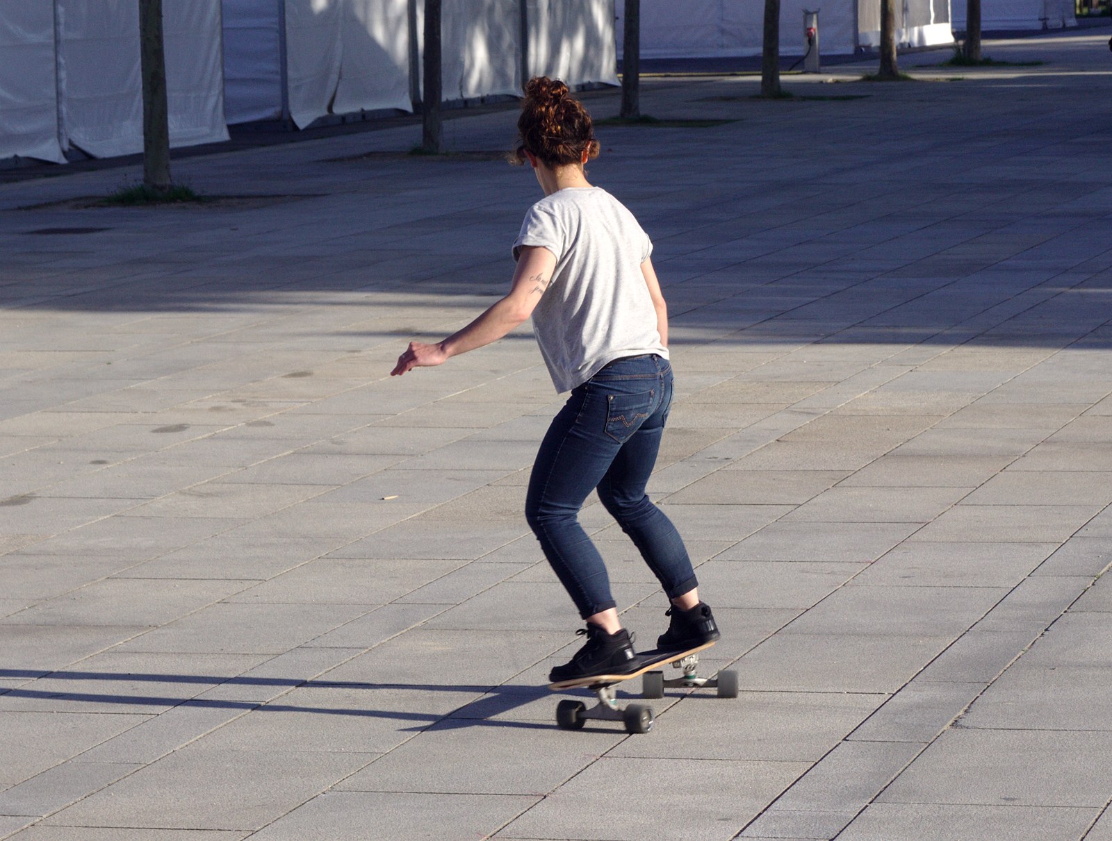Skateuse en train de rouler sur des pavés, pieds placés au-dessus des boulons, buste dans l'axe