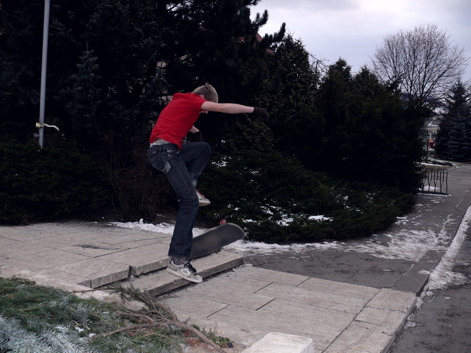 Ado en t-shirt rouge qui claque un ollie sur une marche de trottoir, planche décollée du sol