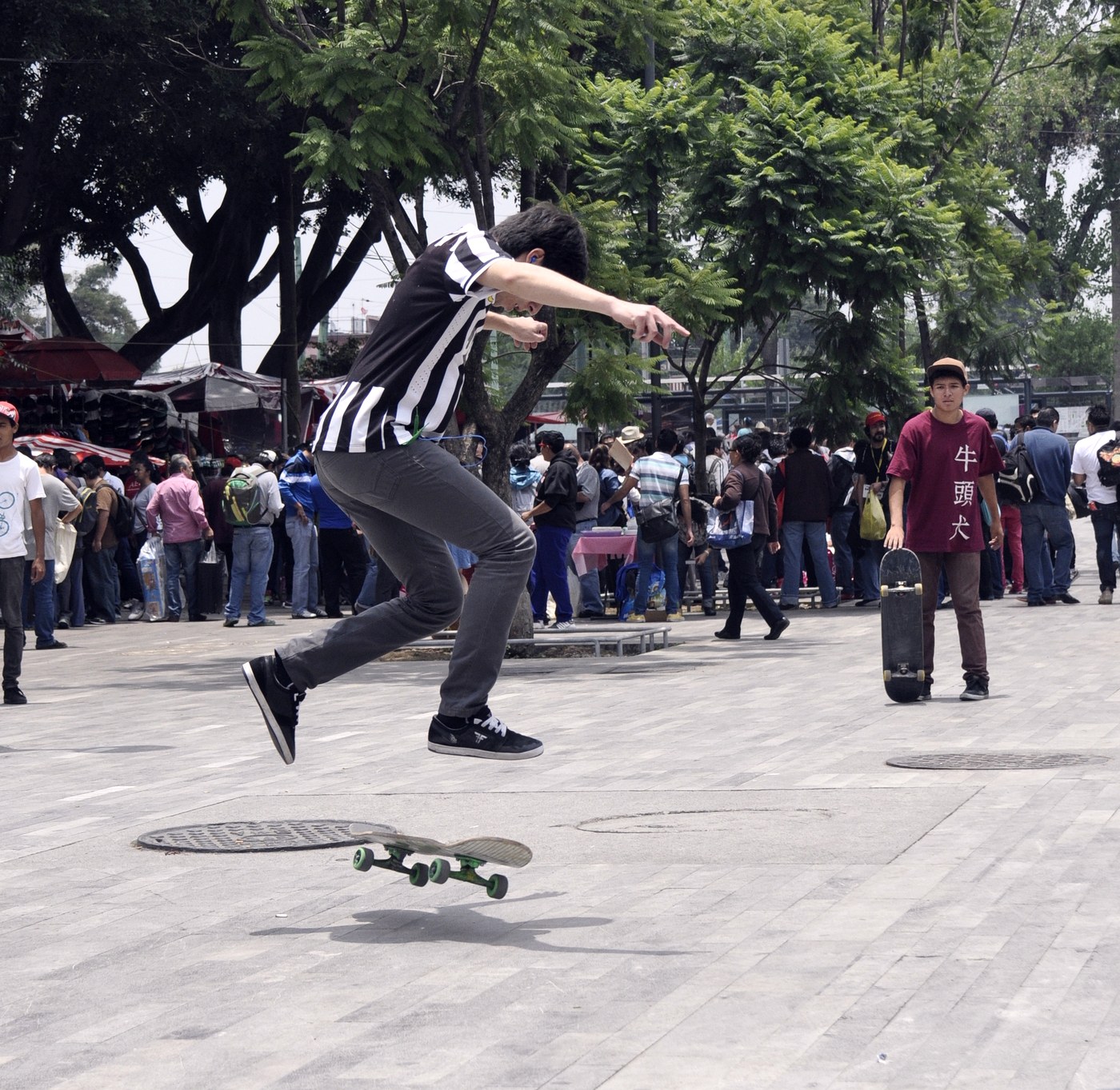Skateur qui rate son trick en pleine rue, la planche partie de côté, devant une foule de passants