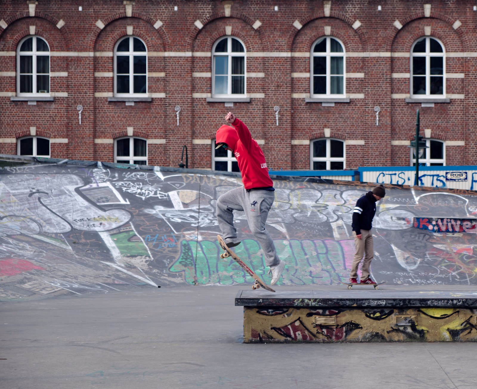 Un skateur envoie un trick sur un ledge de skatepark pendant qu'un autre rider attend son tour derrière