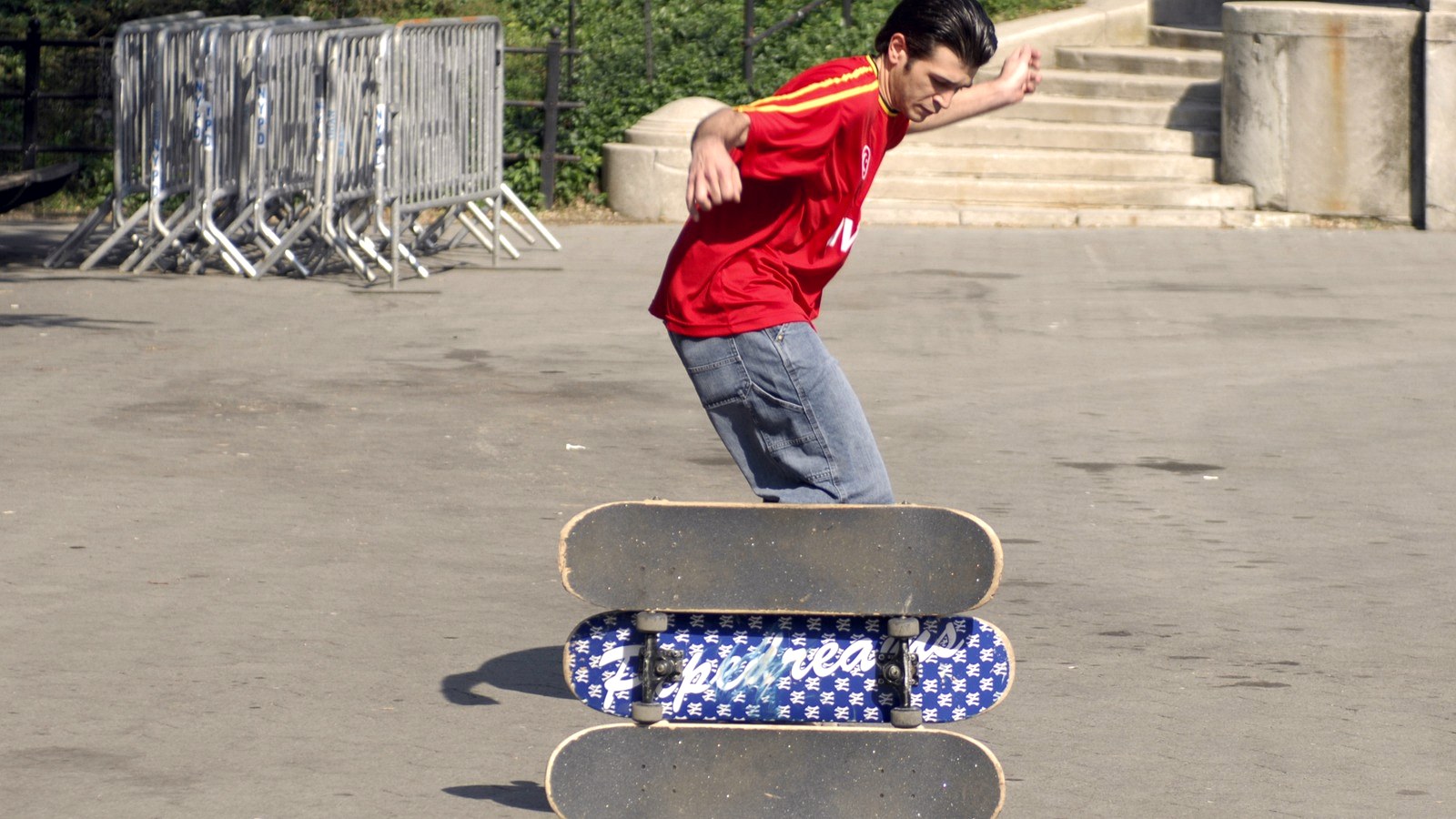 Skateur qui prend son élan pour franchir trois planches empilées, une hauteur de trottoir fabriquée sur du plat