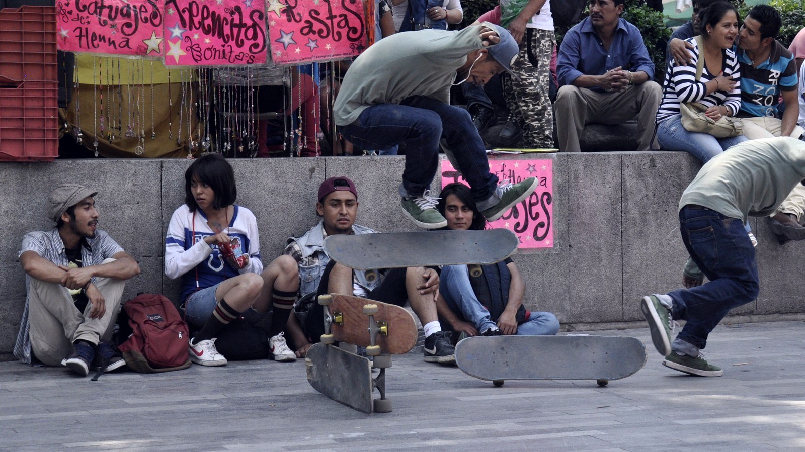 Skateur en plein ollie au-dessus de deux planches devant des spectateurs assis sur une place publique