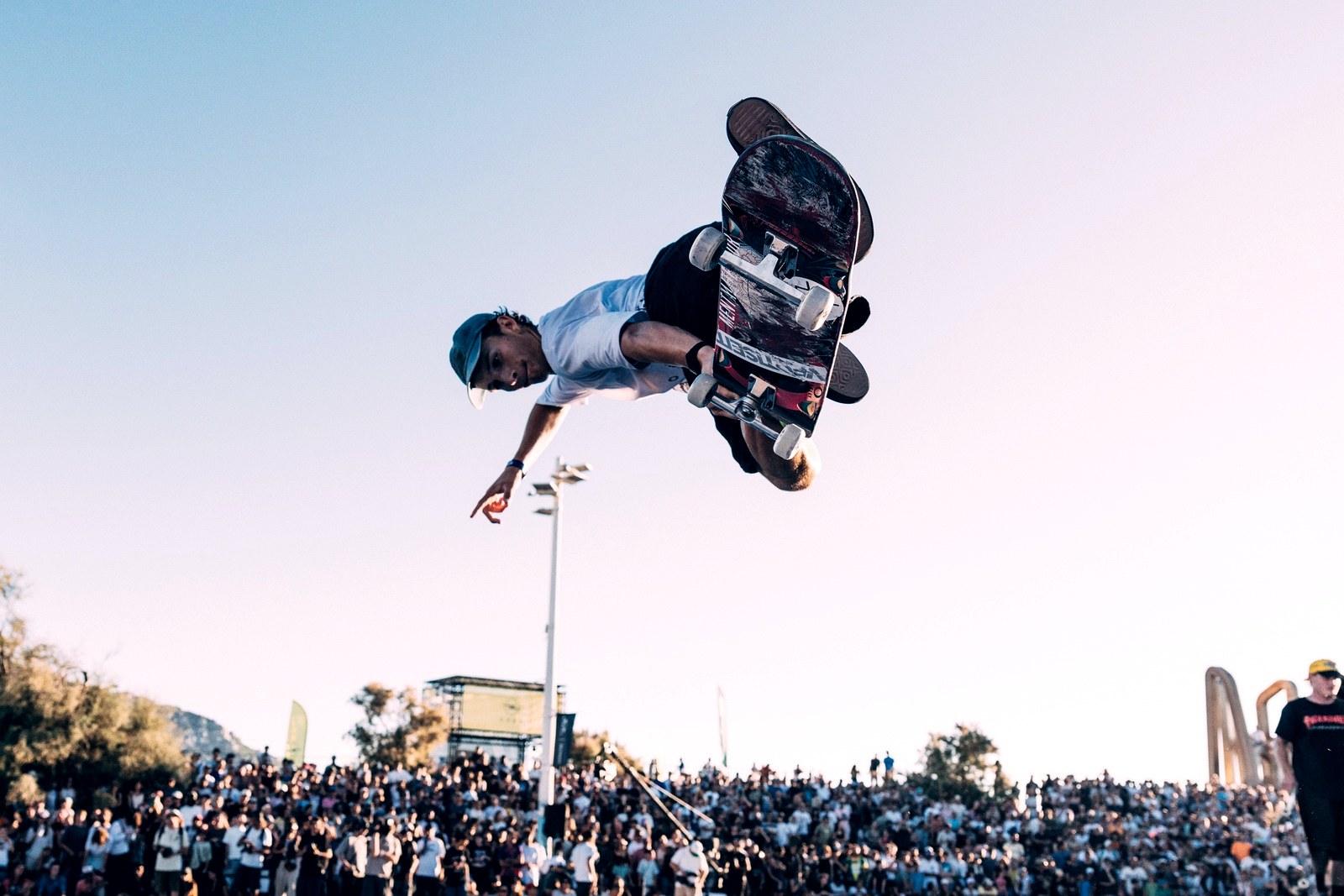 Finale de contest de skate un dimanche après-midi : le rider en plein air au-dessus du bowl devant les tribunes pleines, l'heure qui compte