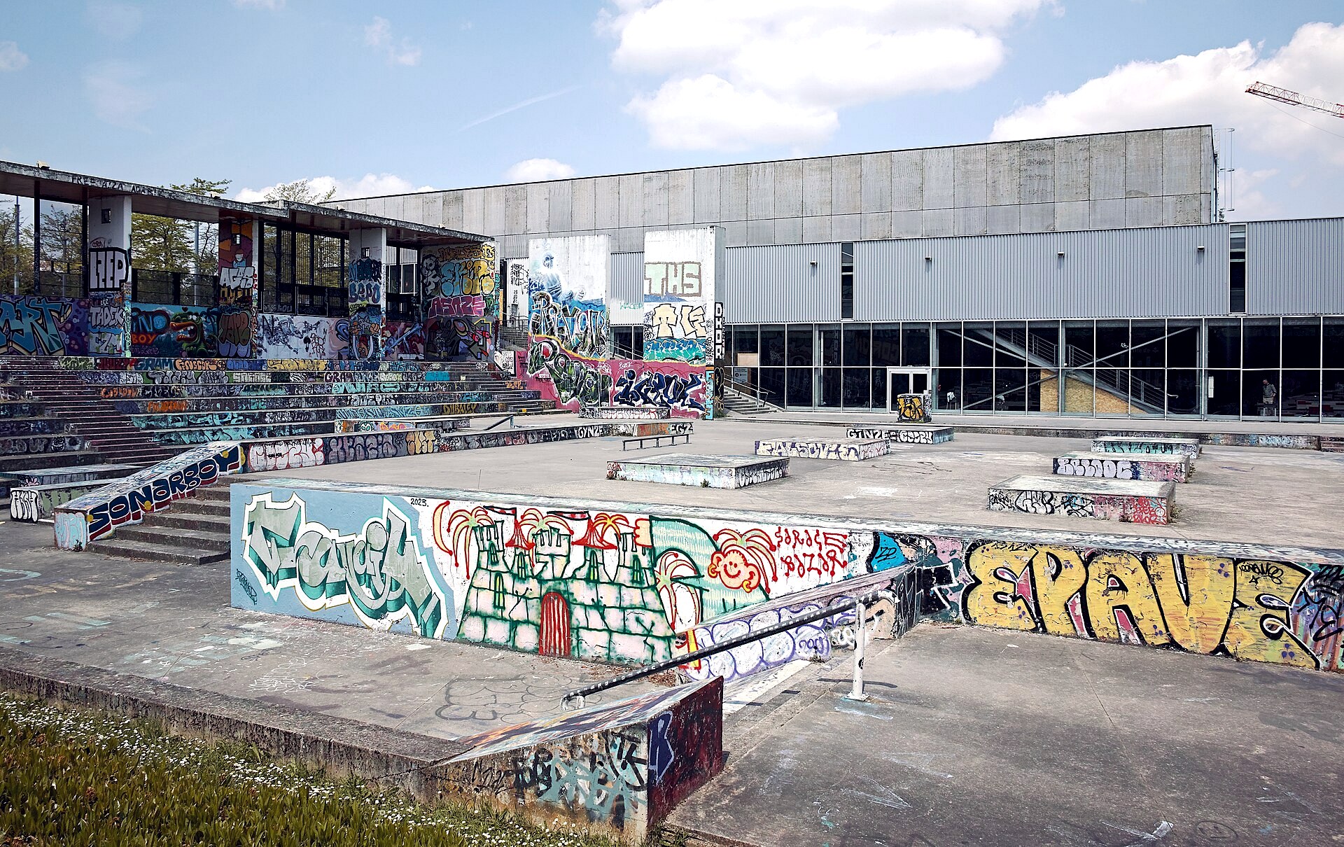 Halle de glisse de Lille : skatepark en béton couvert de graffitis avec sa halle abritée derrière, l'un des rares skateparks français couverts