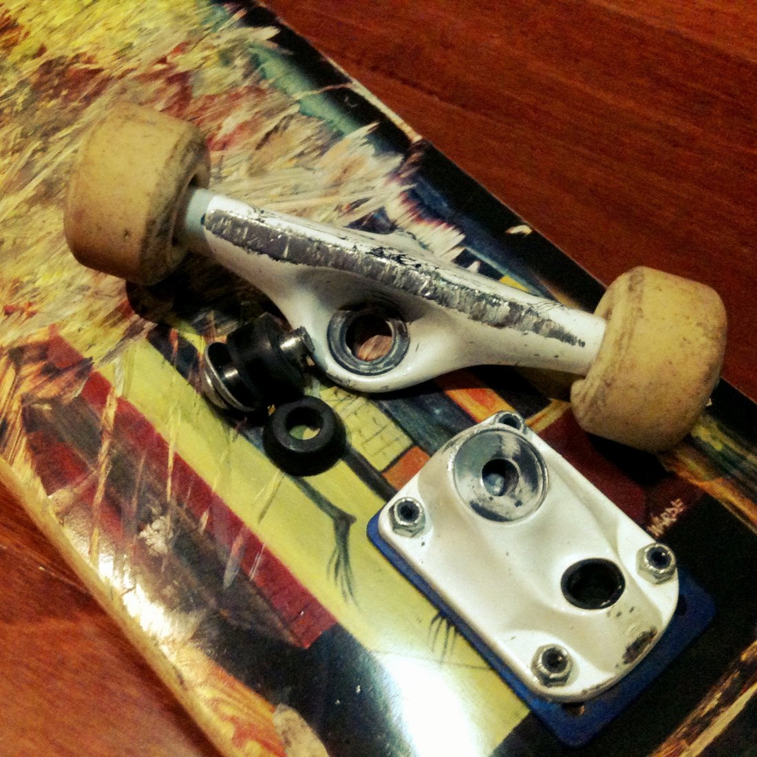 Truck de skate démonté avec un kingpin cassé, les bushings et l'écrou posés à côté sur le deck