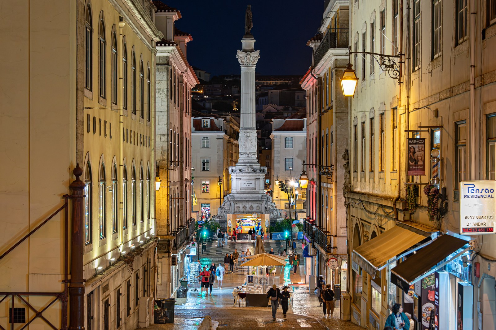 Rue pavée de calçada descendant vers le Rossio à Lisbonne la nuit, sol mouillé et brillant
