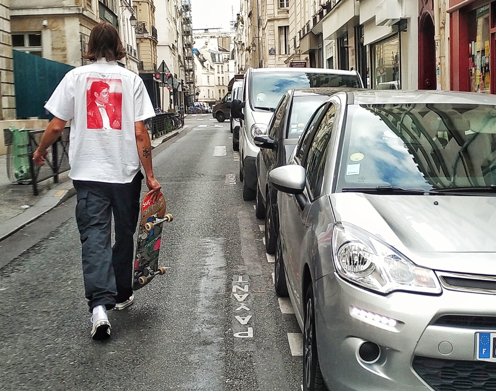 Skateur marchant planche à la main dans une rue de Paris, entre deux spots avant la session