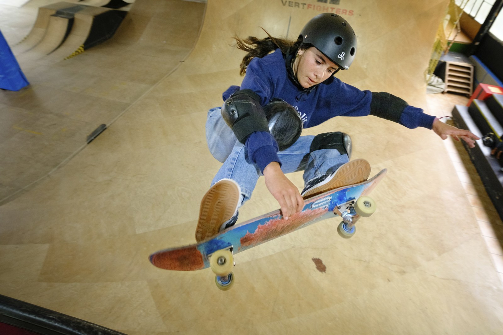 Jeune skateuse casquée et protégée en action sur une mini-rampe en bois, la surface idéale pour apprendre le rock to fakie