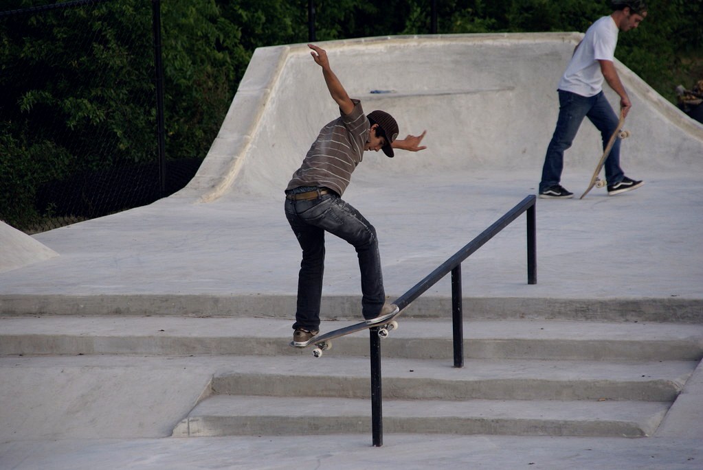 Skateur en boardslide sur un flat bar bas de skatepark, planche en travers de l&rsquo;obstacle
