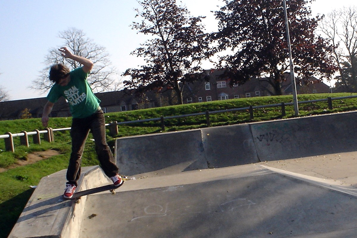 Skateur en noseslide sur un rebord en béton bas de skatepark, seul le nose du deck touche l&rsquo;arête