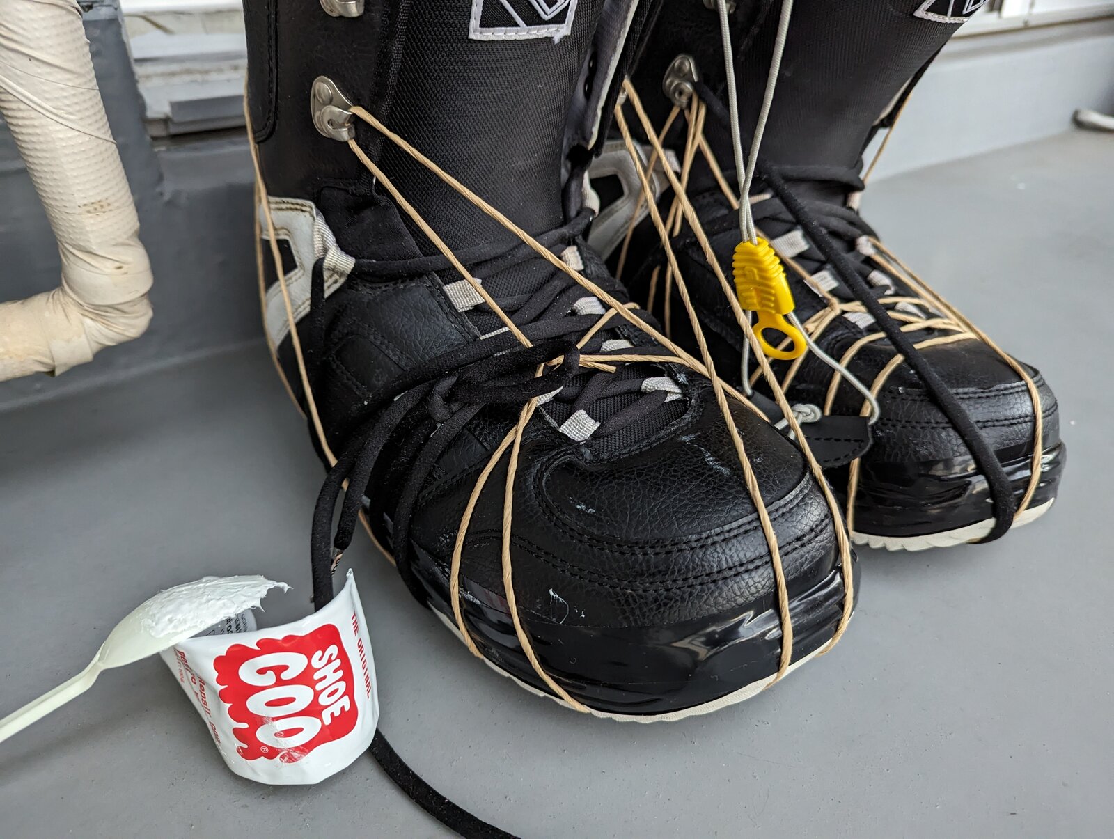 Tube de Shoe Goo ouvert devant une paire de boots réparées, colle étalée sur la pointe