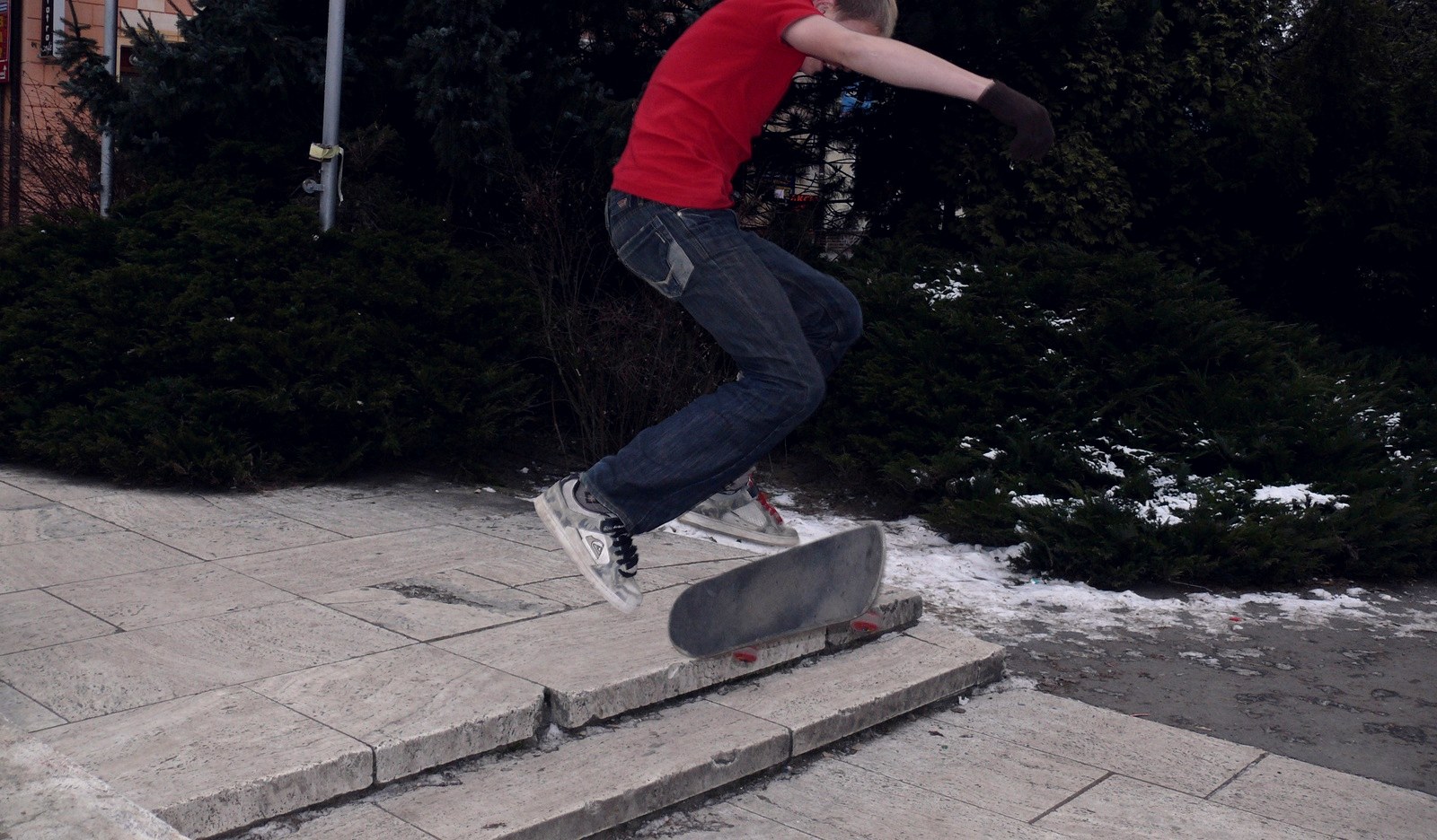 Skateur en plein ollie au-dessus d'une marche, chaussures de skate en suède visibles sur un sol froid et humide