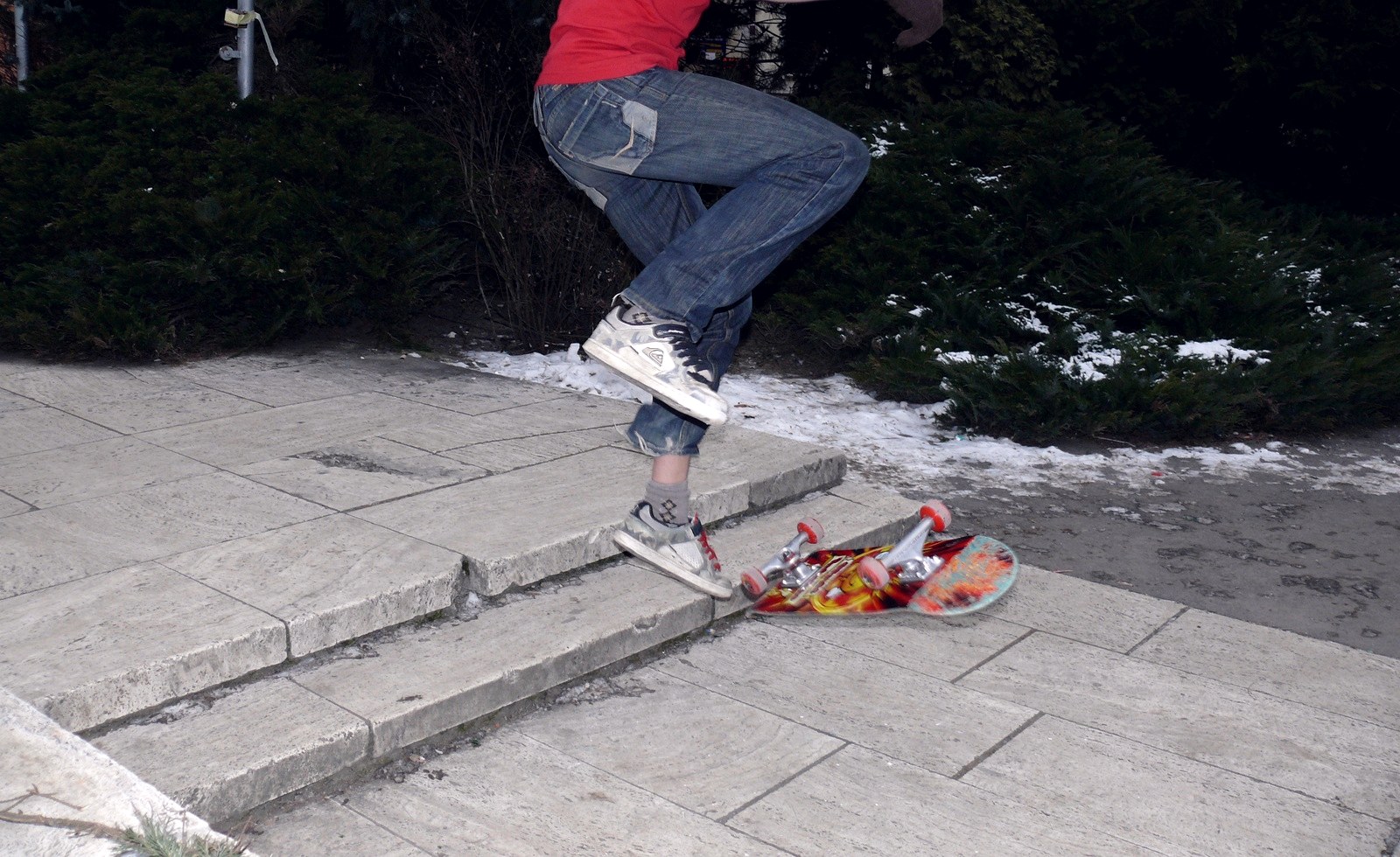 Planche de skate retombée à l'envers, grip contre le béton humide, à côté d'un reste de neige fondante