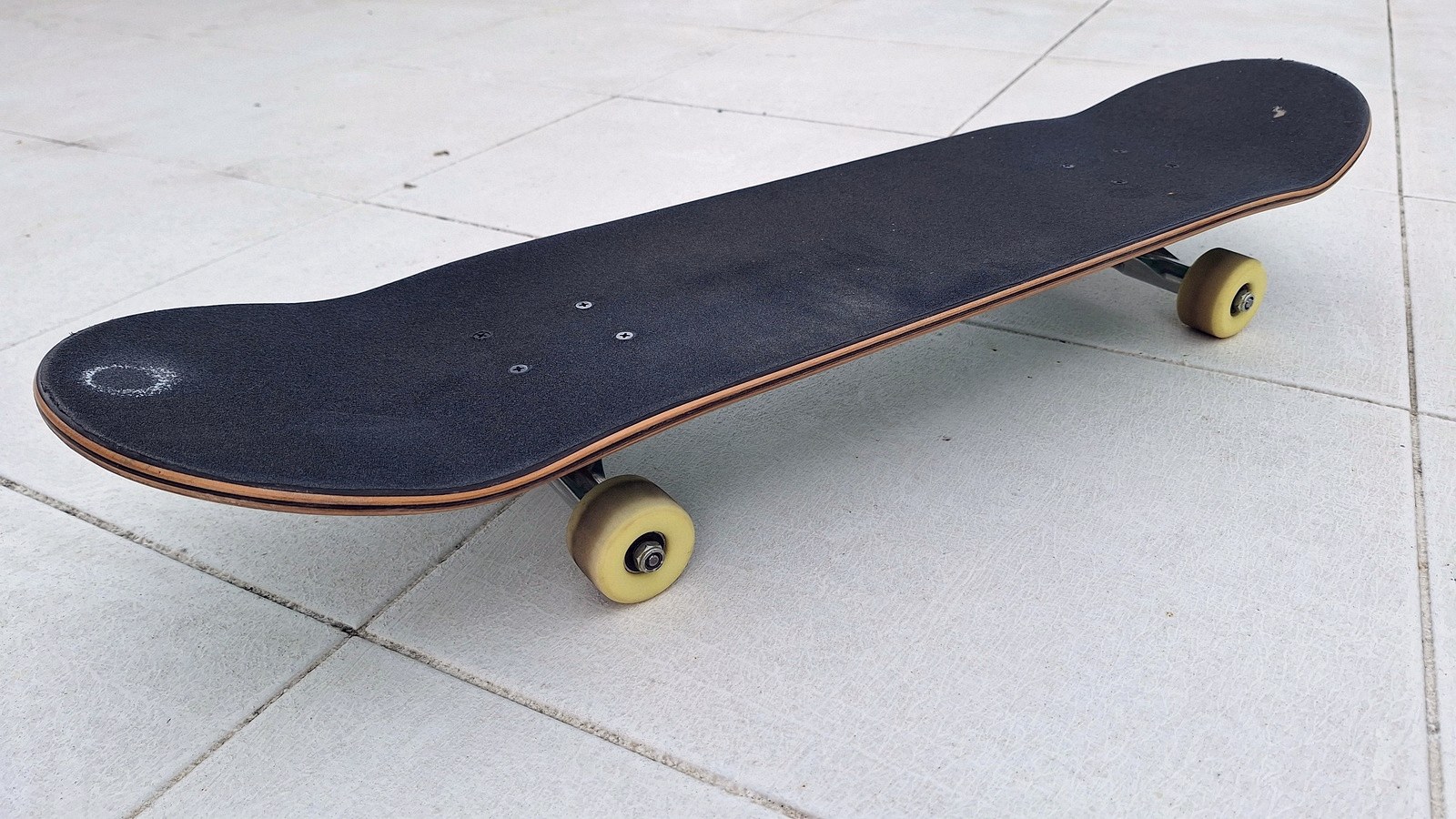 Tranche d'un plateau de skateboard posé au sol, plis d'érable et bois nu visibles sur le bord