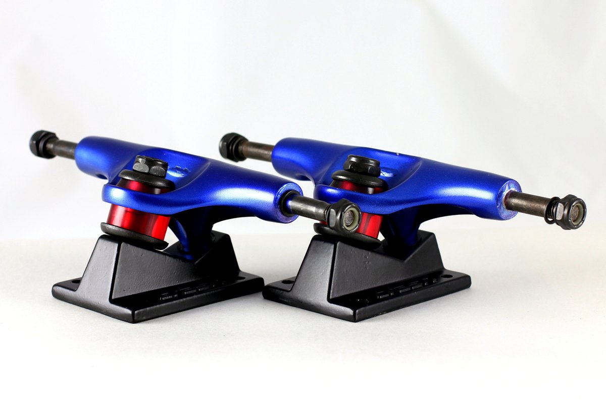 Paire de trucks de skate avec l'écrou du kingpin et les bushings rouges bien visibles, le réglage serré ou lâche se fait là