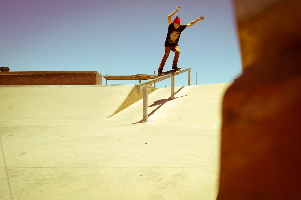 Backside feeble grind sur un rail de skatepark : un seul truck sur le rail, le board en travers, les bras ouverts