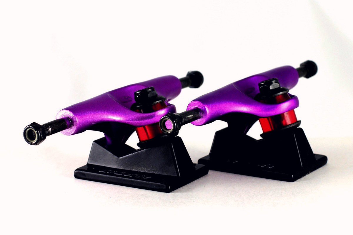 Deux trucks de skate violets avec leur kingpin et leurs bushings rouges avant montage sur le deck