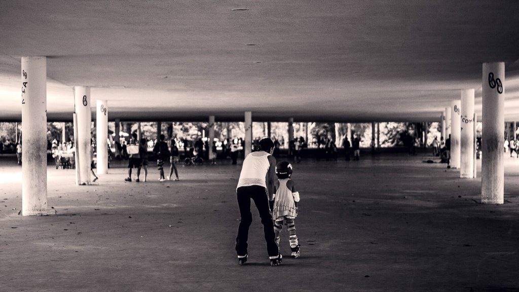 Un adulte apprend à un enfant casqué à rouler sous la Marquise du parc Ibirapuera, le sol où le skate était interdit en 1988